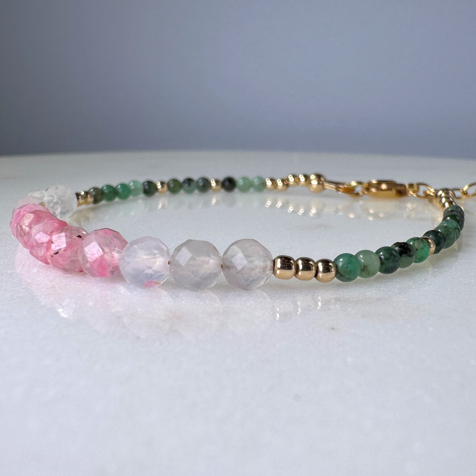 Beaded bracelet with pink, green, and gold beads on a light surface.