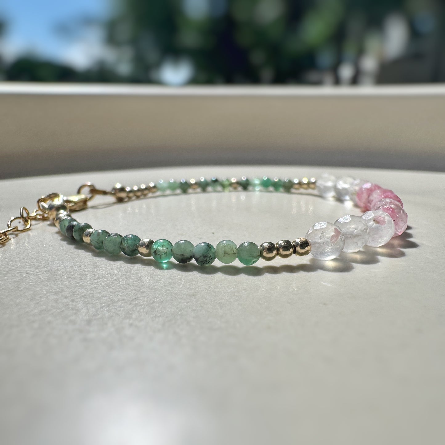 Bracelet with green and pink beads on a light surface with blurred natural background