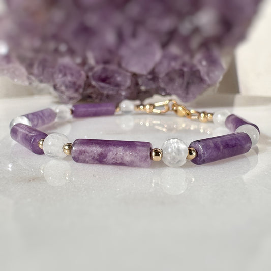 Bracelet with purple and white beads on a white surface with a purple crystal in the background