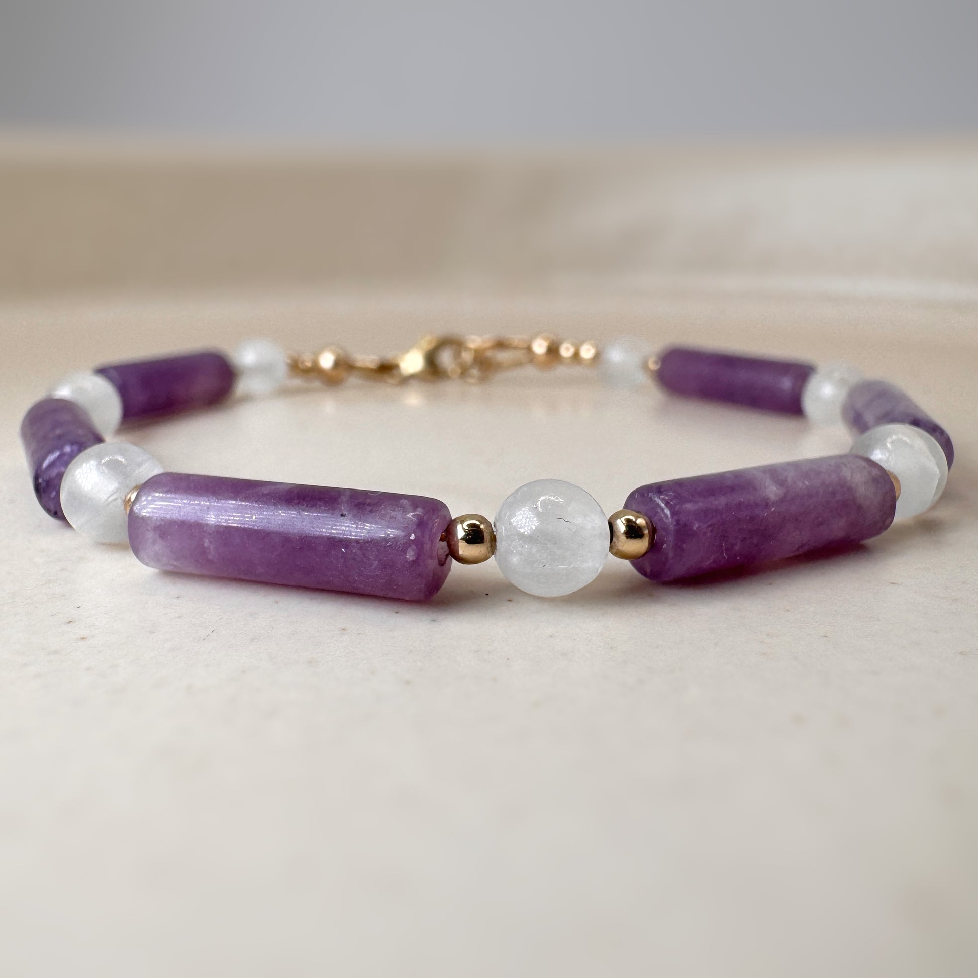 Beaded bracelet with purple, white, and gold beads on a light background
