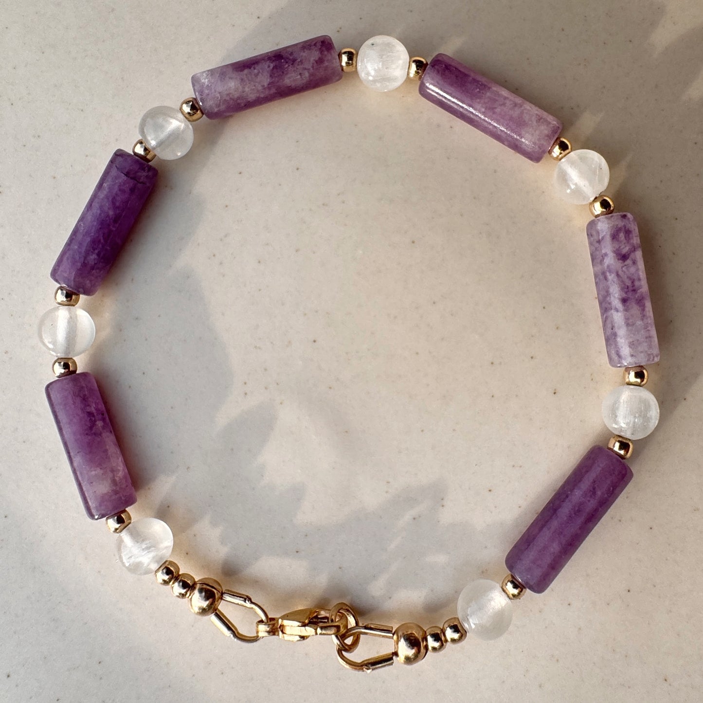 Bracelet with purple beads and gold chain on a light background
