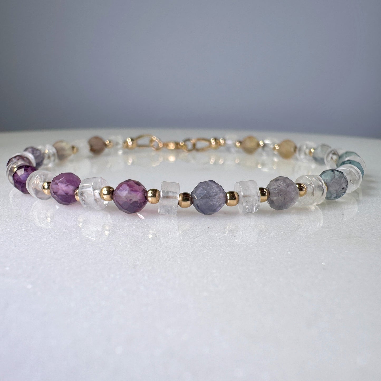 Beaded bracelet with purple, clear, and gold beads on a white surface.