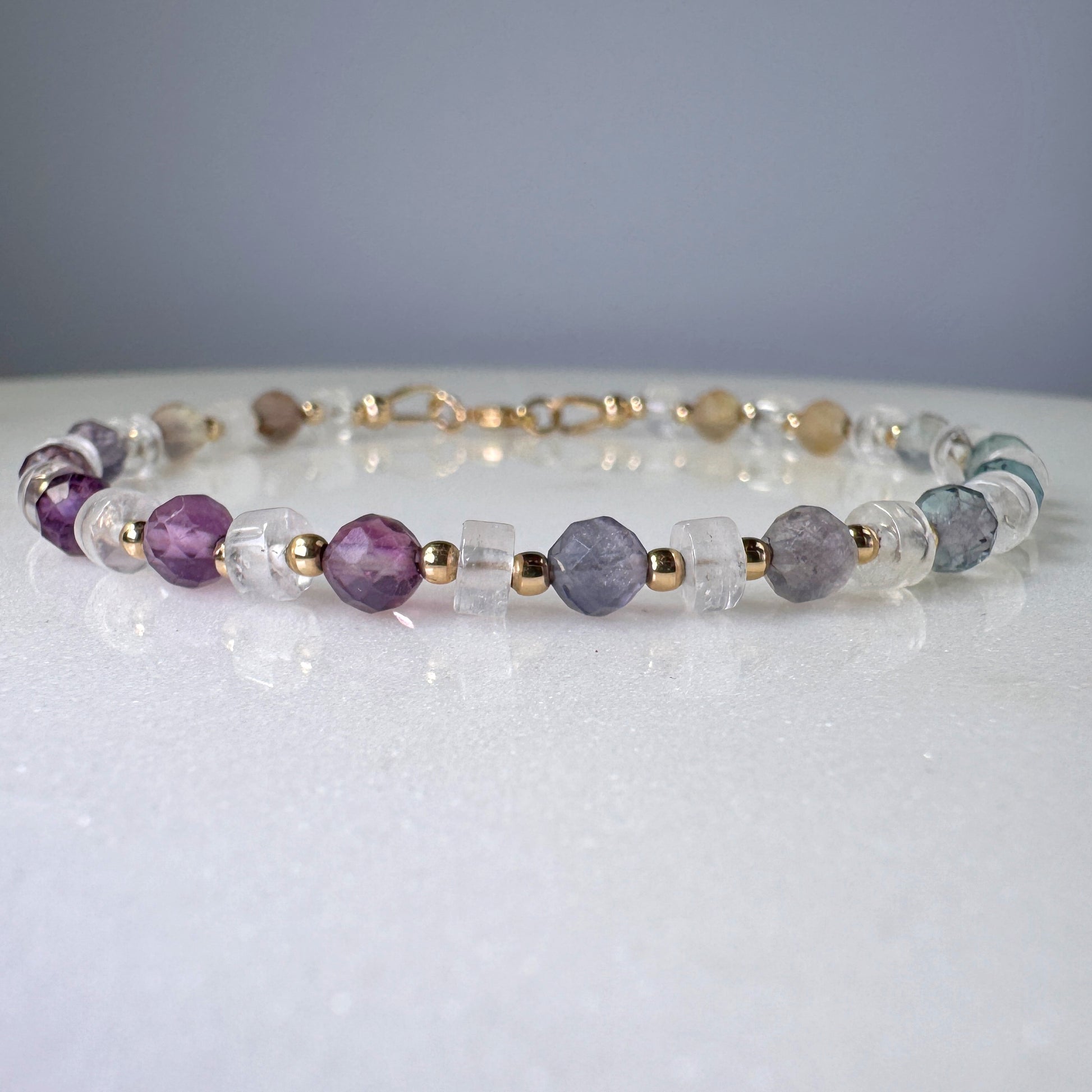 Beaded bracelet with purple, clear, and gold beads on a white surface.