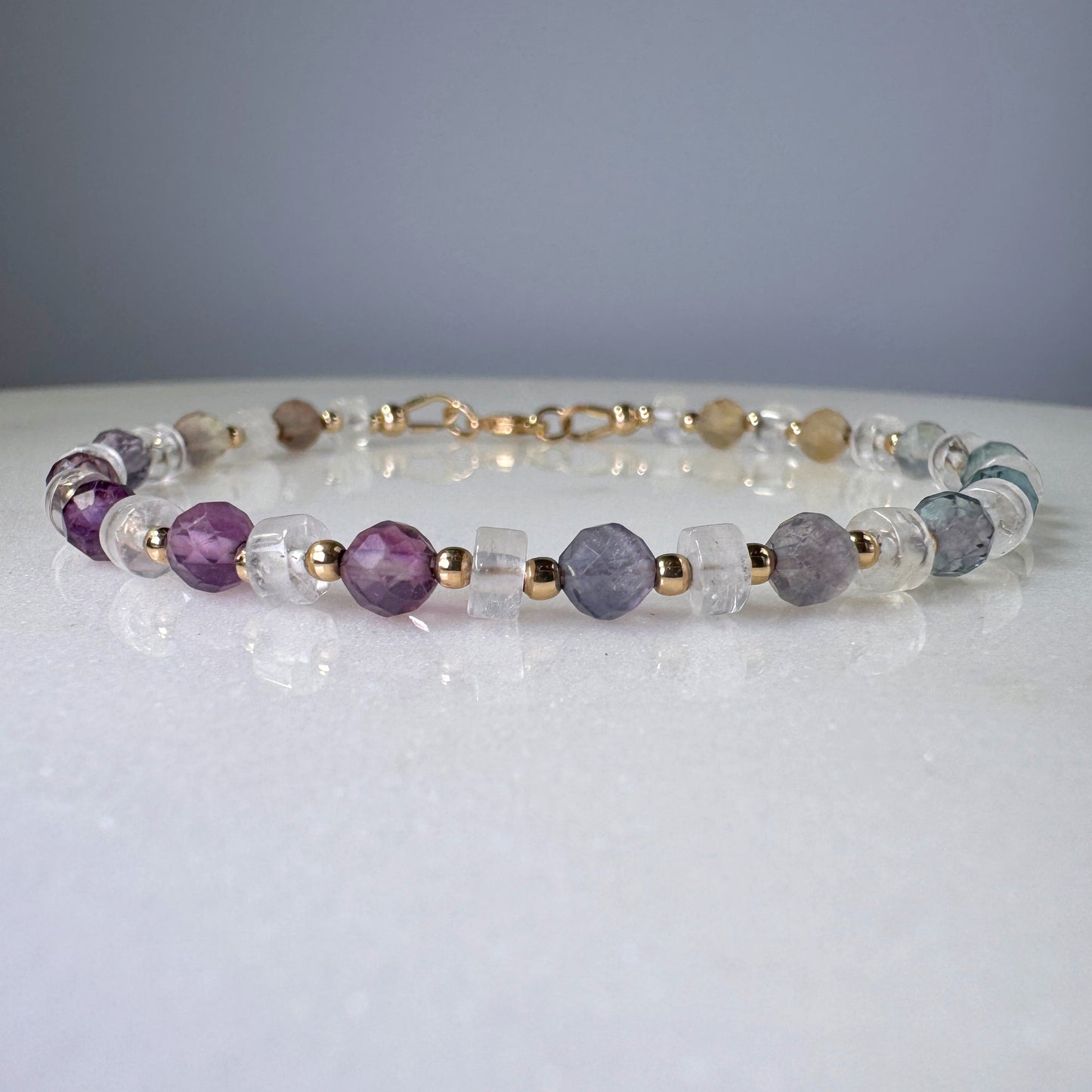 Necklace with purple, clear, and gold beads on a white surface with a gray background