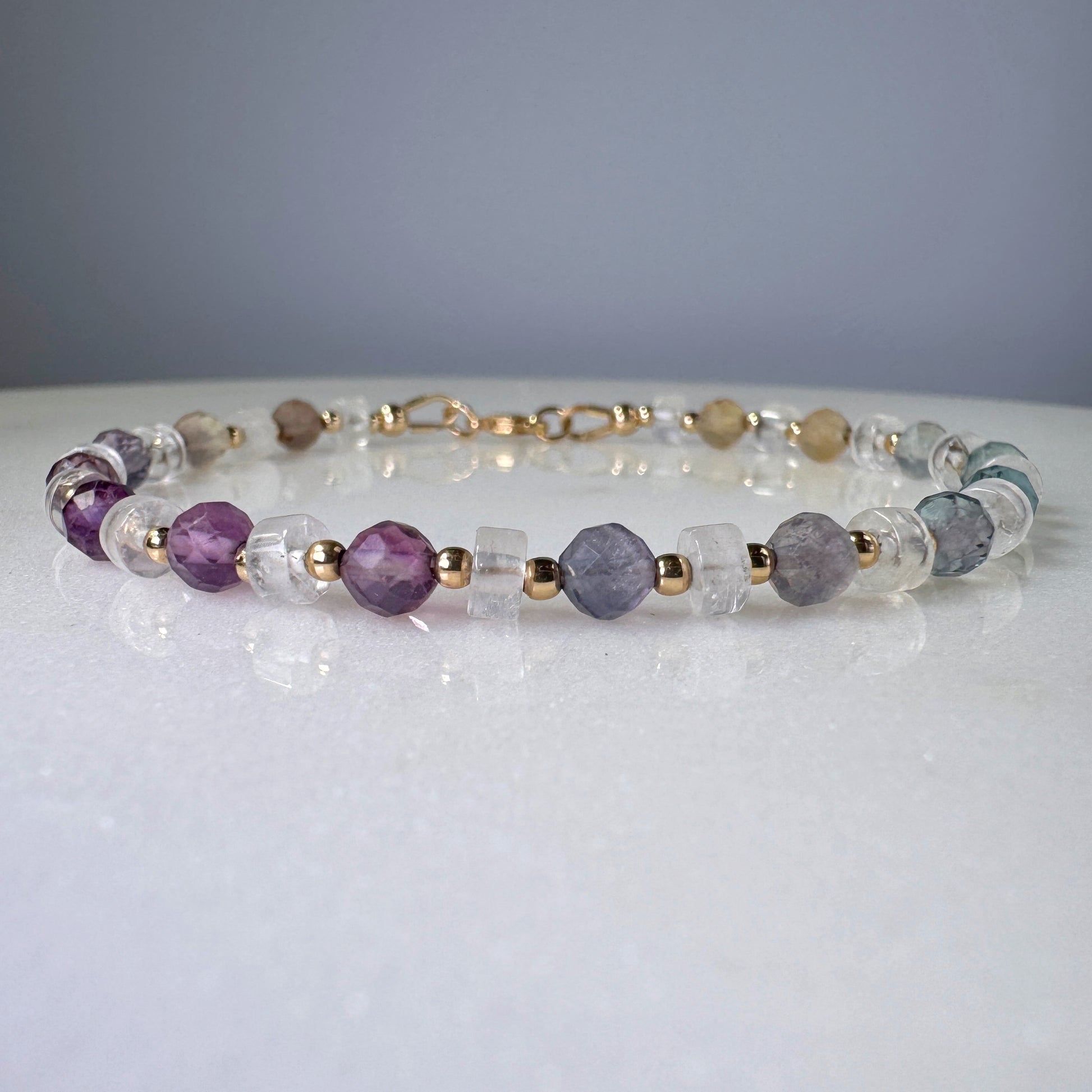 Necklace with purple, clear, and gold beads on a white surface with a gray background